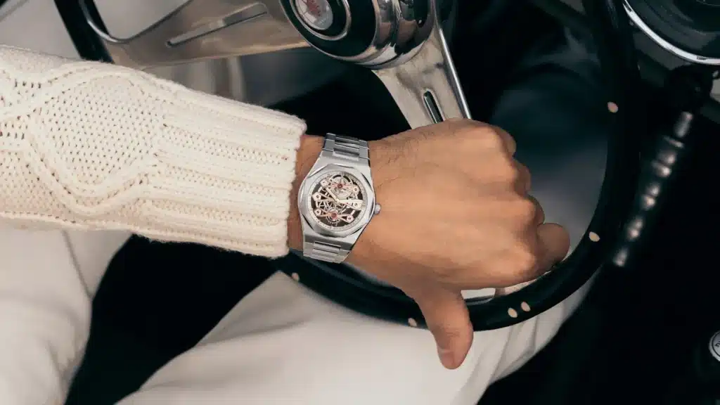 Al volante Il Laureato con ponti in oro rosa al polso di un guidatore, con la mano sul volante di un'auto d'epoca